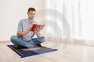 Muslim man reading Koran on prayer rug indoors