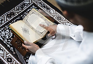 Muslim man sitting on a prayer rug reading Quran