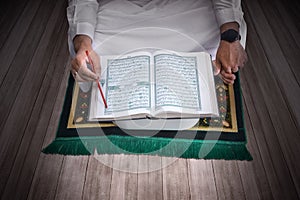 A Muslim man sitting and reading the Quran on the prayer rug