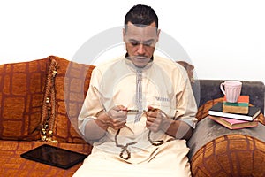 Muslim man using misbaha to keep track of counting in tasbih and drinking coffee, reading books