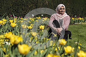 Muslim mature woman sitting relaxed on the grass with flowers in a beautiful spring day in a Park of London