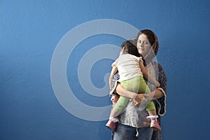 Muslim mother embraced slept little girl in front of blue wall background