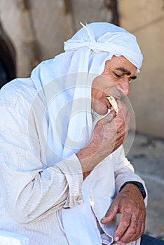 Muslim old man in ghutrah or keffiyeh or kufiya eat pita bread with hummus-traditional arab food.
