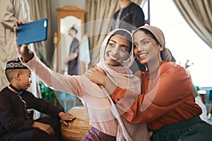 Muslim sisters taking selfies in traditional Islamic head scarf inside a happy family home together. Beautiful young