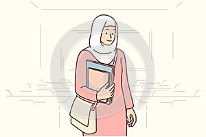 Muslim student girl stands in auditorium with books in hands, dressed in islamic clothing and chador