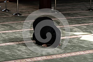 Muslim woman in a black dress with hijab praying in a mosque.