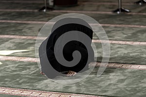 Muslim woman in a black dress with hijab praying in a mosque.