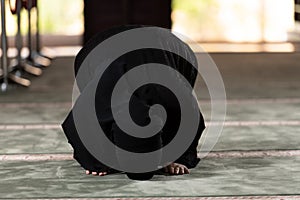 Muslim woman in a black dress with hijab praying in a mosque.