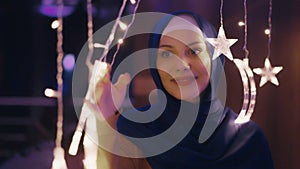 Muslim Woman in Blue Hijab Touching Hanging Moon and Star Decor and Smiling