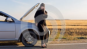 Muslim woman calling help phone near open hood of car