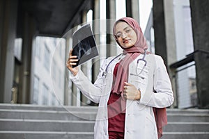 Muslim woman doctor, standing on the stair of modern clinic with x-ray scan image in hands