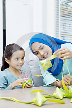 Muslim woman guiding her daughter in weaving ribbon ketupats