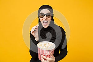 Muslim woman in hijab black clothes 3d imax glasses watch movie film hold bucket popcorn, eat pop corn isolated on