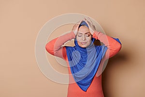 Muslim woman in hijab, rubbing temples, curing tension headache, suffers from migaine, grimacing in pain, beige backdrop