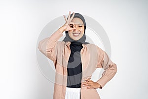 muslim woman in hijab showing oke gesture with hands imitating binoculars