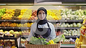 Muslim woman in hijab walks with basket of fresh vegetables in the supermarket, slow motion