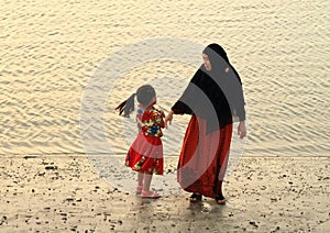 Muslim woman with little girl walking on beach