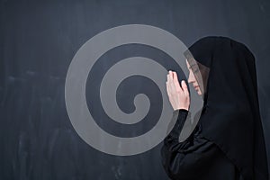 Muslim woman making traditional prayer to God in front of black chalkboard