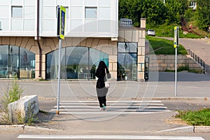 A Muslim woman national clothes walks along pedestrian crossing hurrying