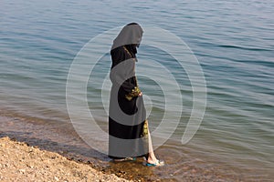 A Muslim woman in national clothes wets her feet