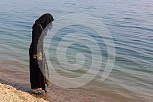 A Muslim woman in national clothes wets her feet in the sea