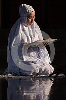 Muslim woman in prayer cap and arabic clothes reading holy quran book praying to Allah