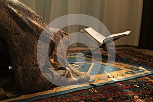Muslim woman praying for Allah muslim god at room near window. Hands of muslim woman on the carpet praying in traditional wearing