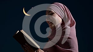 A Muslim woman reads the Quran against the background of a the moon and star