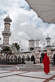 Muslim woman in a red cape standing in a courtyard of the Masjid Jamek Mosque in Kuala Lumpur in Malaysia