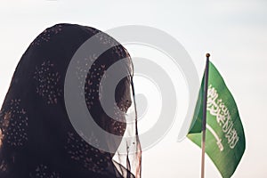 Muslim woman in scarf with Saudi Arabia flag of at sunset.