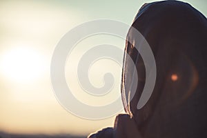 Muslim woman in scarf on sunset sky background.