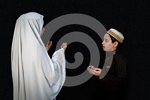 Muslim woman and son pilgrims in white traditional clothes, praying at Kaaba in Makkah