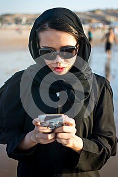 Muslim woman texting on the beach