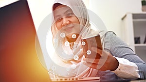 Muslim woman using phone and laptop computer with internet of things graphic icons, mobile wireless technology