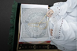 Muslim woman in a veil sitting while raised hands and praying with prayer beads