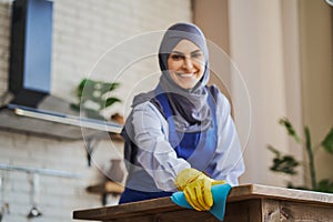 Muslim woman wearing apron and gloves while cleaning a house