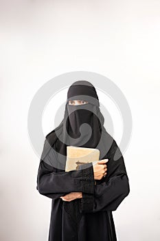 muslim woman wearing a black hijab and long dress holding al qur'an