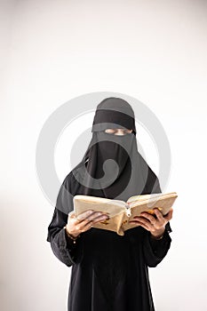 muslim woman wearing a black hijab and long dress reading al qur'an