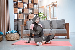 a Muslim woman wearing a hijab sportswear sits cross-legged on the floor on a mattress