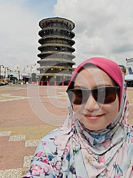 Muslim woman wearing sunglasses is taking a self-portrait with the The Leaning Tower of Teluk Intan, a famous landmark in Perak,