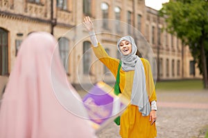 Muslim woman wearing yellow dress waving her friend