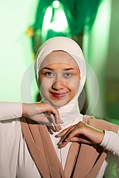 a Muslim woman in a white headscarf and white clothes poses with her hands without the slightest makeup on her face and smiles