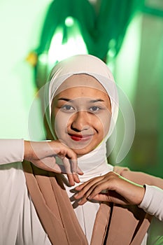 a Muslim woman in a white headscarf and white clothes poses with her hands without the slightest makeup on her face and smiles