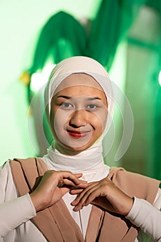 a Muslim woman in a white headscarf and white clothes poses with her hands without the slightest makeup on her face and smiles