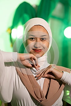 a Muslim woman in a white headscarf and white clothes poses with her hands without the slightest makeup on her face and smiles