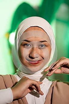 a Muslim woman in a white headscarf and white clothes poses with her hands without the slightest makeup on her face and smiles