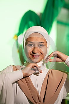 a Muslim woman in a white headscarf and white clothes poses with her hands without the slightest makeup on her face and smiles