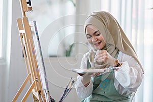Muslim young female artist painting on canvas at home. Hobby and leisure concept.