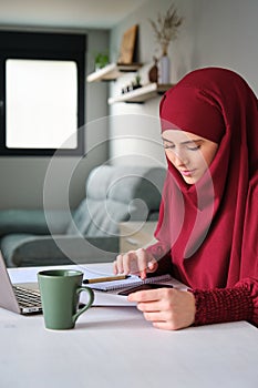 Muslim young woman in hijab managing home finance.