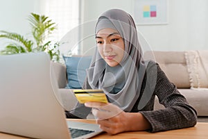 Muslim young women wear hijab are buying online with a credit card while sitting living room at home. Beautiful woman is using
